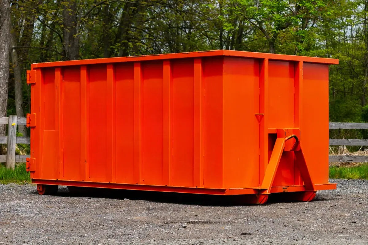 Small orange roll-off dumpster on gravel