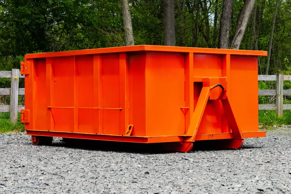 Orange roll-off dumpster with rear door on a gravel pad