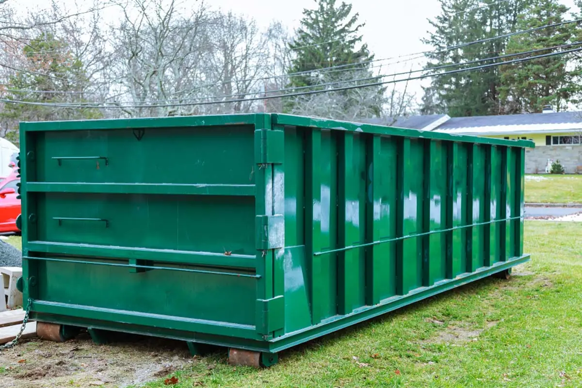 Green 30-yard roll-off dumpster set on boards in a residential yard