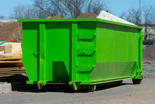 Green roll-off dumpster on a construction site next to lumber