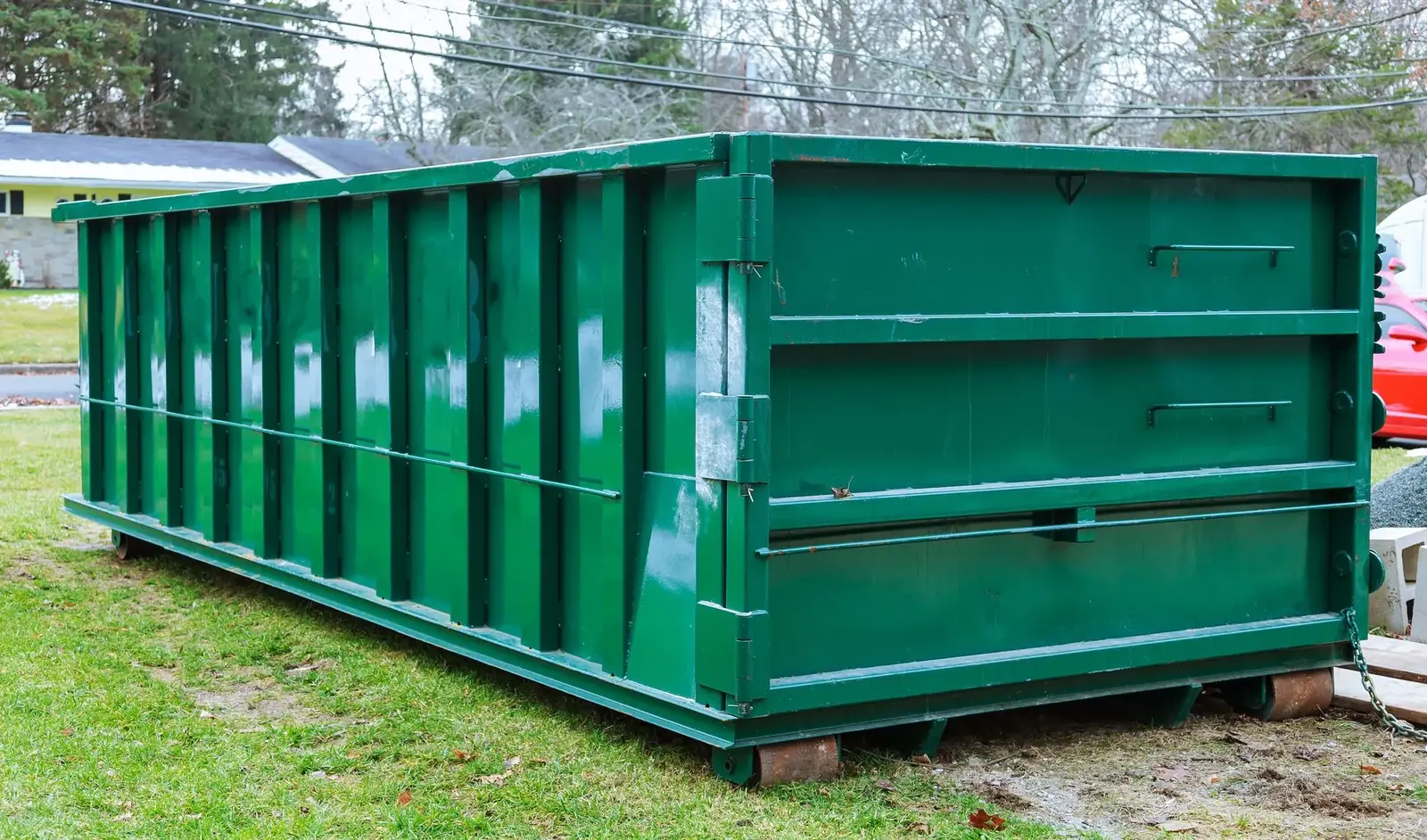 Green 30-yard roll-off dumpster resting on wooden boards beside homes
